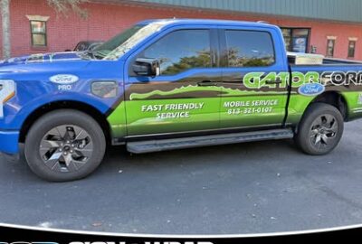 Blue and green wrapped pickup truck advertising B2B Sign & Wrap Resource with mobile sign service and contact info on the side panel.